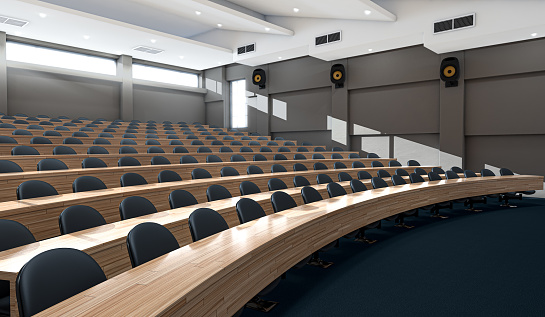An interior of an empty lecture hall auditorium with rows of curved wooden desks and chairs lit by morning sunlight - 3D render