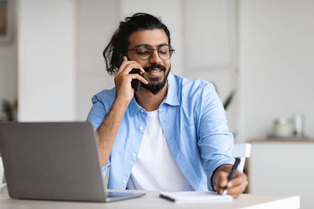 istock Young Arab Male Entrepreneur Talking On Cellphone And Taking Notes In Office 1295751524