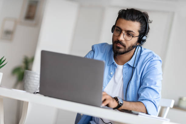 istock Young Arab Male Hotline Operator In Headset Working With Laptop In Office 1295752351