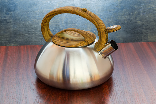 Stainless steel stovetop kettle with steam whistle built-in in spout on a wooden table