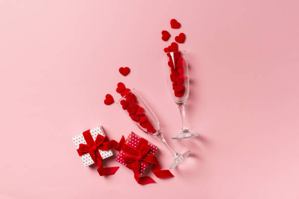 istock Two glasses with red hearts and gift flat lay on pink background 1295754621
