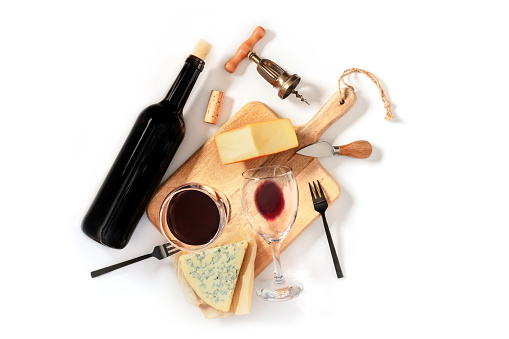 Wine and cheese tasting, overhead flat lay shot on a white background, with a vintage corkscrew, a wine bottle, and two glasses