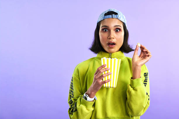 Studio shot of a beautiful young woman eating popcorn against a purple background