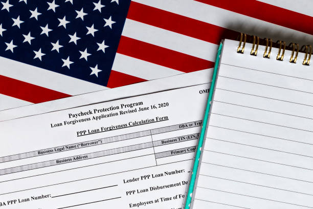 istock close-up of paycheck protection program loan forgiveness application form revised topview, on a background of United States flag. paycheck protection program new round. 1295756230