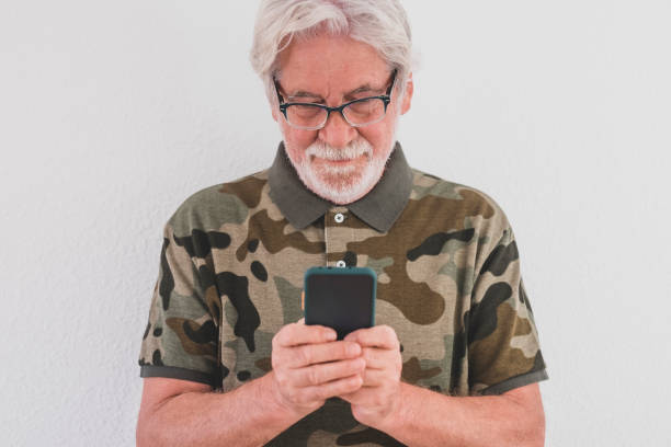 istock Attractive senior white-haired man with glasses types a text message on smartphone standing on a white background - older people appreciate technology 1295756812