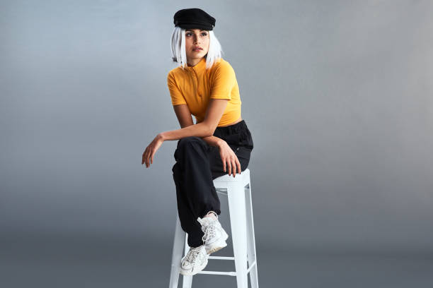 Do you know the history behind the baker boy hat? Studio shot of a beautiful young woman sitting on a stool against a grey background short weave hairstyles stock pictures, royalty-free photos & images
