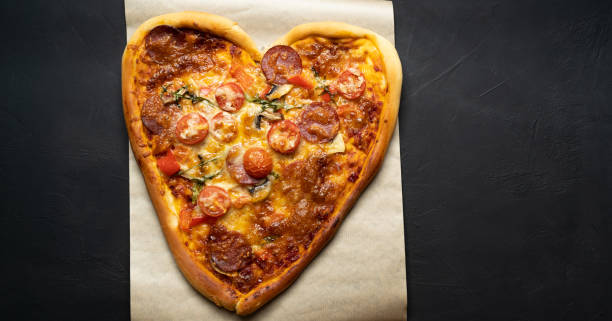 istock Heart shaped pizza for Valentine's Day on black isolated background. 1295760548