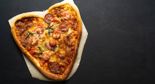 istock Heart shaped mozzarella pizza for Valentine's Day on black isolated background. 1295760552