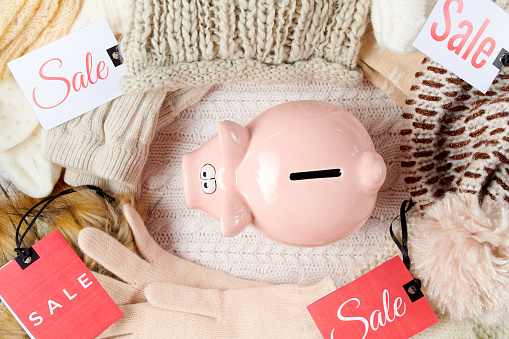 winter flat lay with piggy bank, mittens, hats, winter clothes and sale tag on white knitted background.