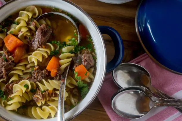 fresh cooked beef noodle soup in a vintage pot with spoons on table background