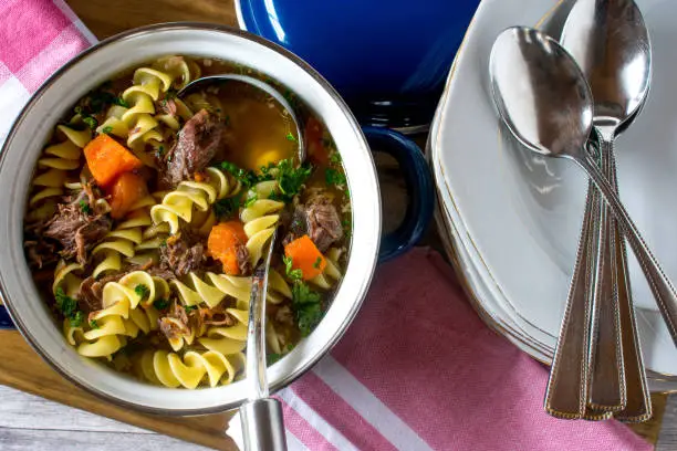 fresh cooked beef stew with spiral noodles in a retro style pot with plates and spoon from above