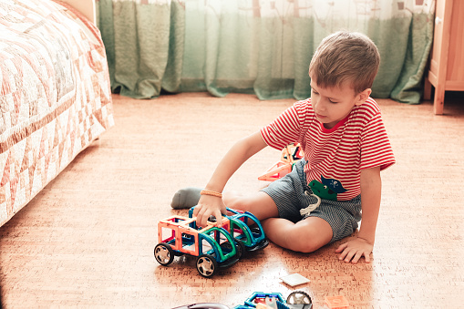 A boy plays with magnetic constructor in children room sitting on cork floor