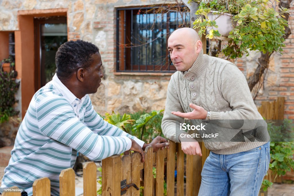 Smiling men chatting near wooden wicket Neighbor conversation. Two smiling men breezily chatting near wooden wicket of rural house Neighbor Stock Photo