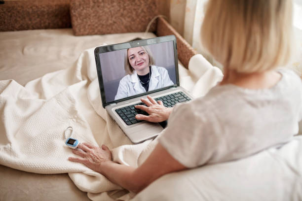 Old woman in bed looking at screen of laptop and consulting with a doctor online at home, telehealth Old woman in bed looking at screen of laptop and consulting with a doctor online at home, telehealth services during lockdown, distant video call, modern tech healthcare application oxygen photos stock pictures, royalty-free photos & images