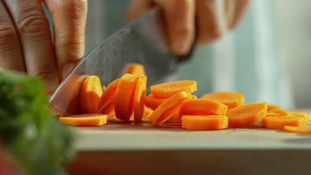 Carrot being sliced on a wooden board