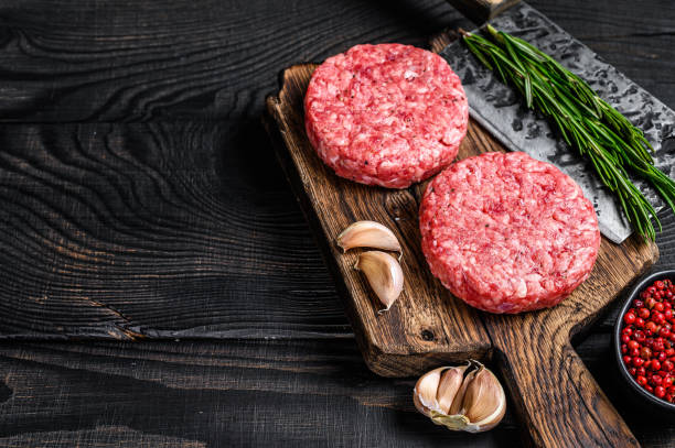 raw steak cutlets with mince beef meat and rosemary on a wooden cutting board with meat cleaver. black wooden background. top view. copy space - ground beef imagens e fotografias de stock