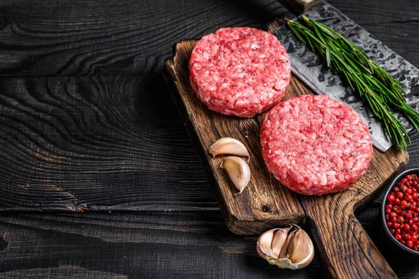 costlets de bife cru com carne de carne de picadinho e alecrim em uma tábua de corte de madeira com cutelo de carne. fundo de madeira preta. vista superior. copiar espaço - cutlet meat steak veal - fotografias e filmes do acervo