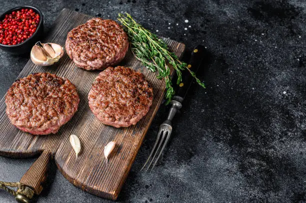 Photo of BBQ grilled beef meat patties for burger from mince meat and herbs on a wooden board. Black background. Top view. Copy space