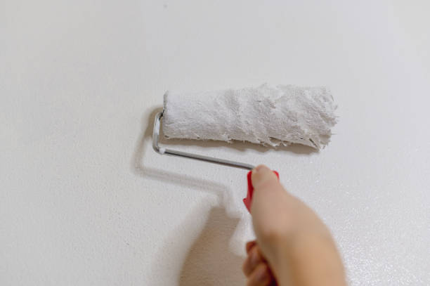 istock Unrecognizable hand holding paint roller painting with white dye in wall. 1295776971
