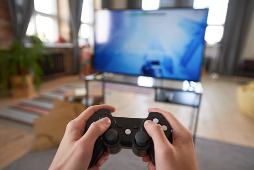 Close-up of gamer holding joystick and playing video game on big screen of TV at home
