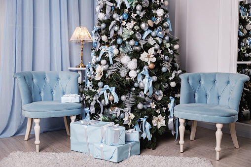 Beautifully packaged blue presents under the Christmas tree and blue armchair