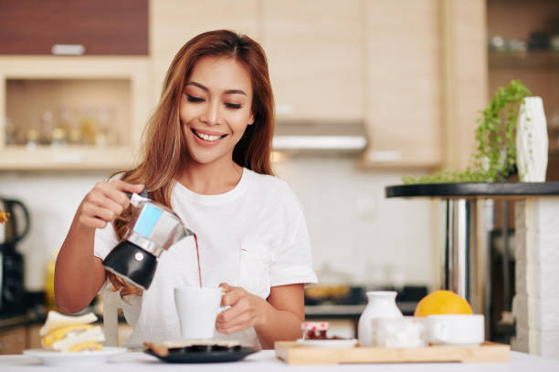 Woman pouring herself coffee Portrait of beautiful young Asian woman pouring herself a cup of coffee when standing at kitchen table hot vietnamese women pictures stock pictures, royalty-free photos & images