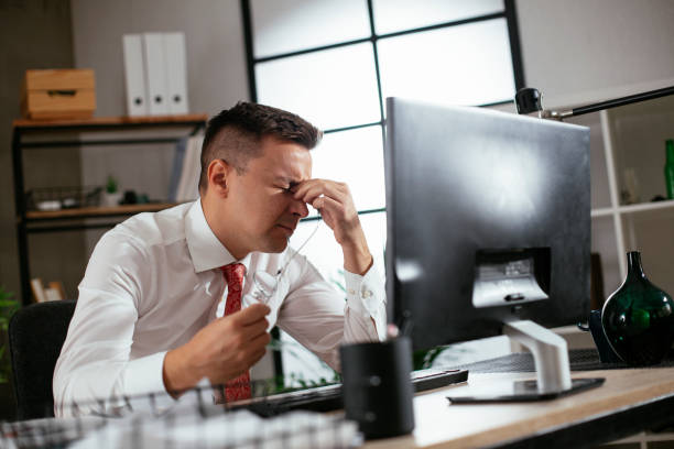 istock Tired man sitting at office desk working on laptop computer. 1295780242