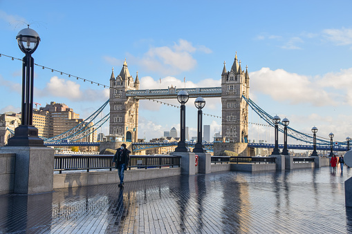 London, United Kingdom - December 15 2020: A man with a protective face mask walks past Tower Bridge during the coronavirus crisis.