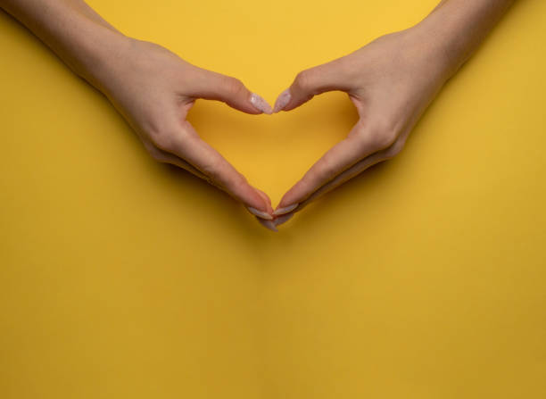istock heart making woman's hands with manicure on yellow background, top view 1295782938