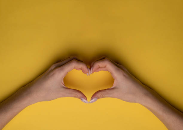 istock heart making woman's hands with manicure on yellow background, top view 1295782972