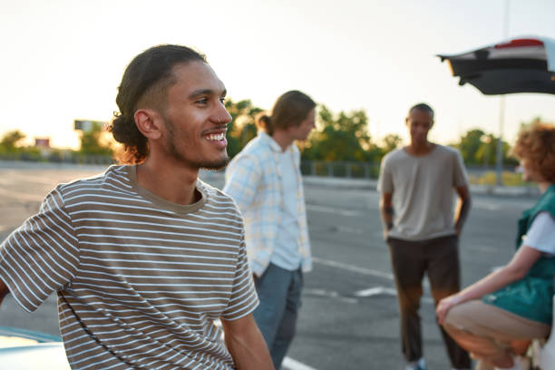 istock A close up of an ordinary dressed dark-skinned latina guy with a piercing smiling standing outside on a parking site with his friends on a background 1295784624