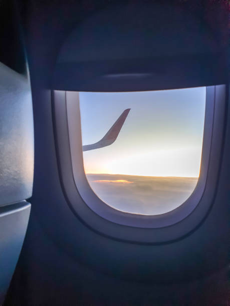 immagine tonica attraverso l'oblò dell'aereo di ala nella luce del tramonto sulle nuvole - window porthole sky cloudscape foto e immagini stock