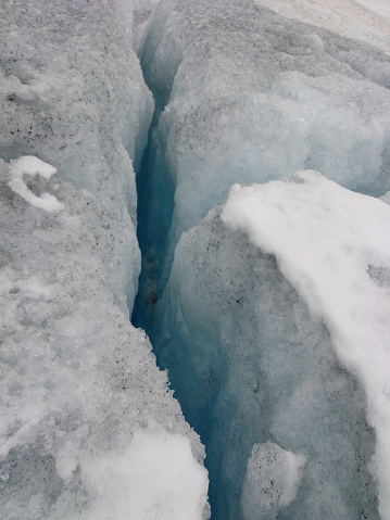 Crack in the ice of a glacier due to global warming and climate change. Melting snow causing sinkhole.