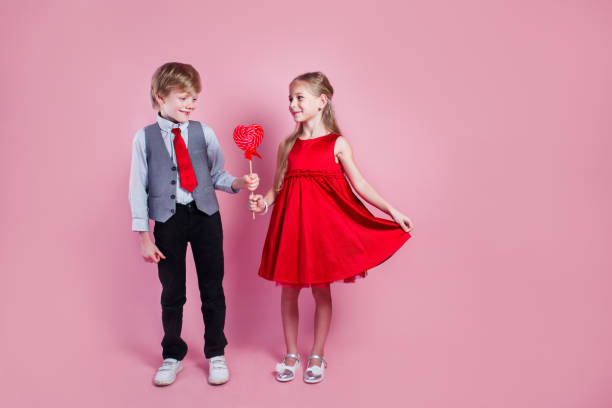 バレンタインデーのコンセプト。ハートの形をしたキャンディーレッドロリポップを持つ小さな男の子と女の子。美しい子供たちはお菓子を食べます。 - child valentines day candy eating ストックフォトと画像