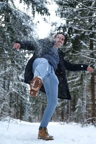 Photo of Young adult having fun kicking snow over the camera looking at the camera