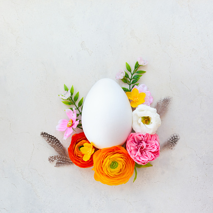Creative Easter concept made of white egg and spring flowers around on vintage background. Flat lay.