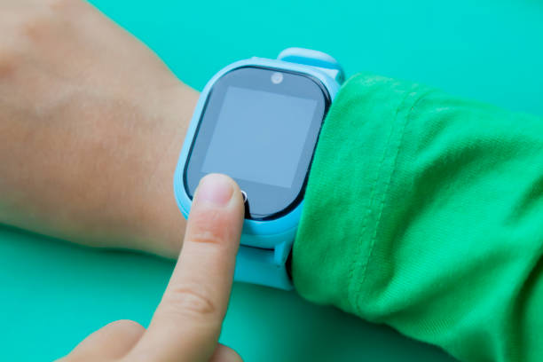 istock boy wants to call his parents on digital clock touching screen with his index finger. Modern children technologies. GPS tracker for kids, child tracking and parental control concept. 1295790147