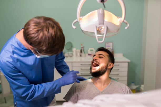 zahnarzt kontrolliert den mund eines bärtigen mannes und spricht freundschaftlich mit ihm - amicably stock-fotos und bilder
