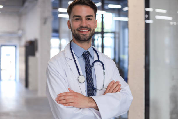 istock Handsome friendly young doctor on hospital corridor looking at camera, smiling. 1295790684
