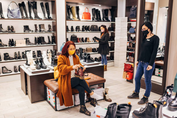 istock Curious woman observing a modern leather boots, before she try them one, while saleswoman sticking around if the customer needs any more help 1295790718