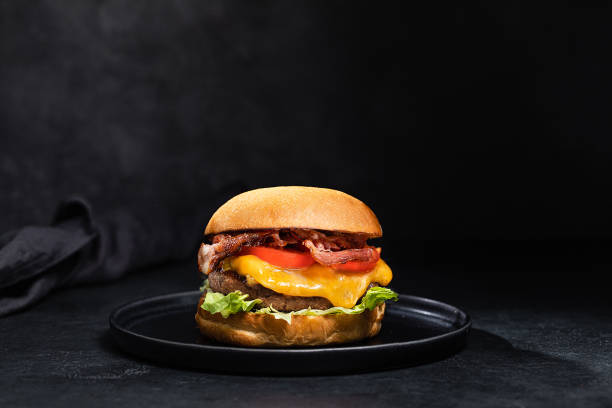 Cheese burger with bacon on black dark background Cheese burger with bacon on black dark background bacon cheeseburger stock pictures, royalty-free photos & images