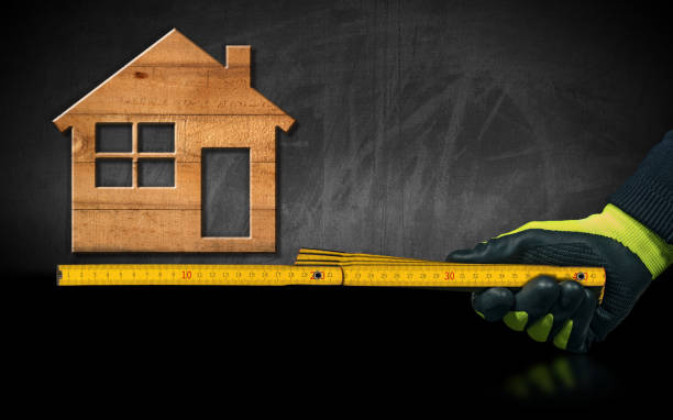 istock Gloved Hand Holding a Wooden Folding Ruler with a Model House on Background 1295801603