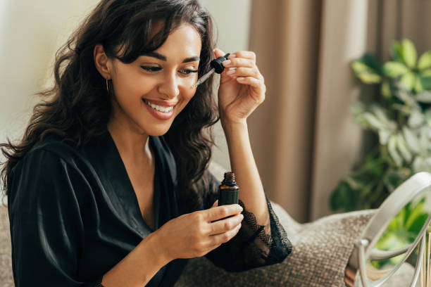 Young smiling woman sitting on a couch applying hyaluronic acid on a face Young smiling woman sitting on a couch applying hyaluronic acid on a face face serum stock pictures, royalty-free photos & images