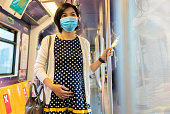 Young Asian Pregnant Woman wearing protective face mask standing in commuter skytrain or metro