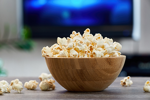 Closeup of a wooden bowl with fresh popcorn, on the background of a home interior with a TV.