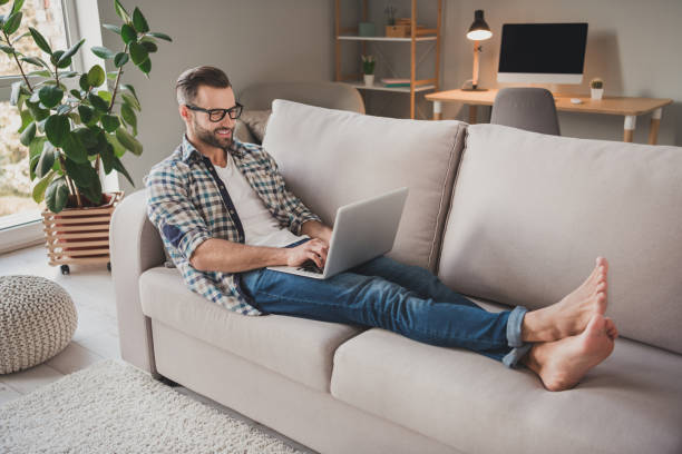 istock Full body profile side photo of young cheerful man sit couch home work distance programmer type email laptop 1295811312