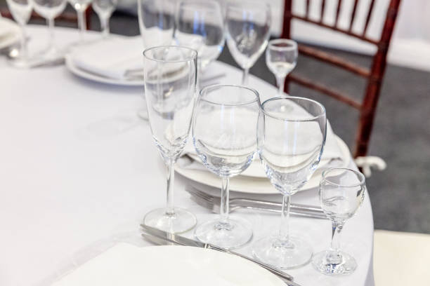 istock Fancy table set for dinner with napkin glasses in restaurant, luxury interior background. Wedding elegant banquet decoration and items for food arranged by catering service on white tablecloth table 1295811359