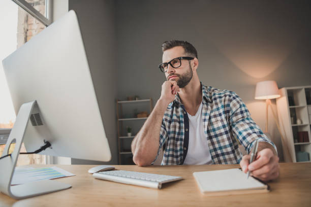 istock Photo of young handsome serious man look computer work distance write notebook plan to-do list indoors 1295812273