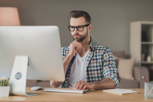 istock Photo of young man serious confident serious look think browse read computer distance work desk indoors 1295812334