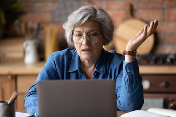 Confused middle aged woman in glasses looking at computer screen. Confused middle aged 60s woman in glasses looking at computer screen, stressed of getting message with bad news. Unhappy mature lady feeling nervous about bad laptop work or poor internet connection. frustration stock pictures, royalty-free photos & images